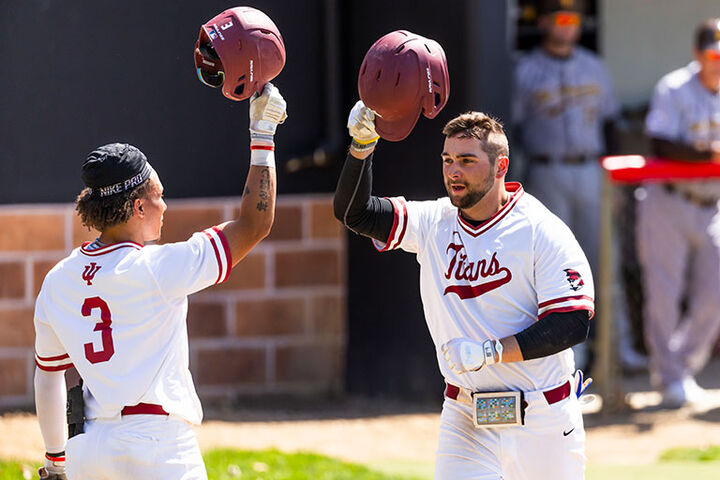 Two baseball players raise and tap their helmets in celebration.